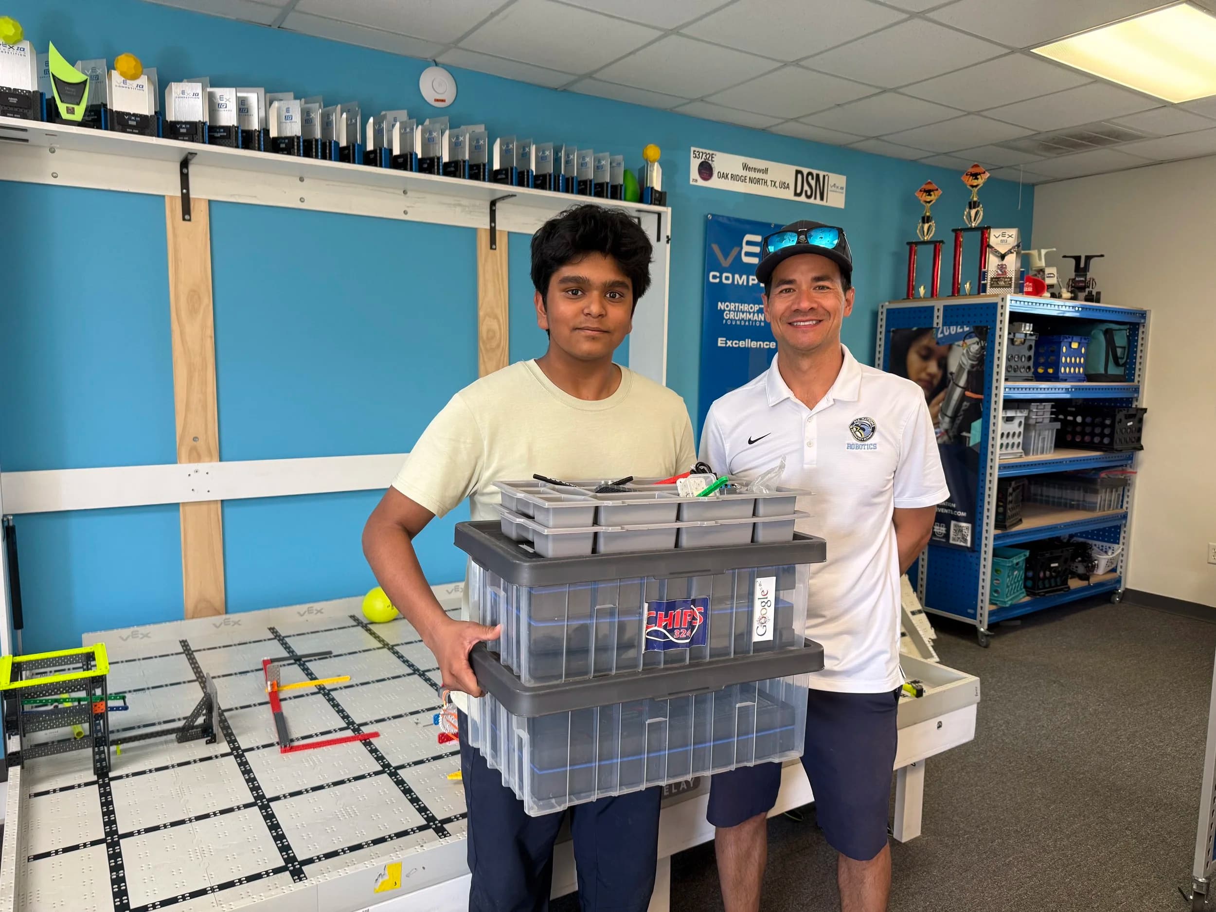 An Up the Ratios volunteer handing two storage bins of VEX parts to a coach at a robotics lab