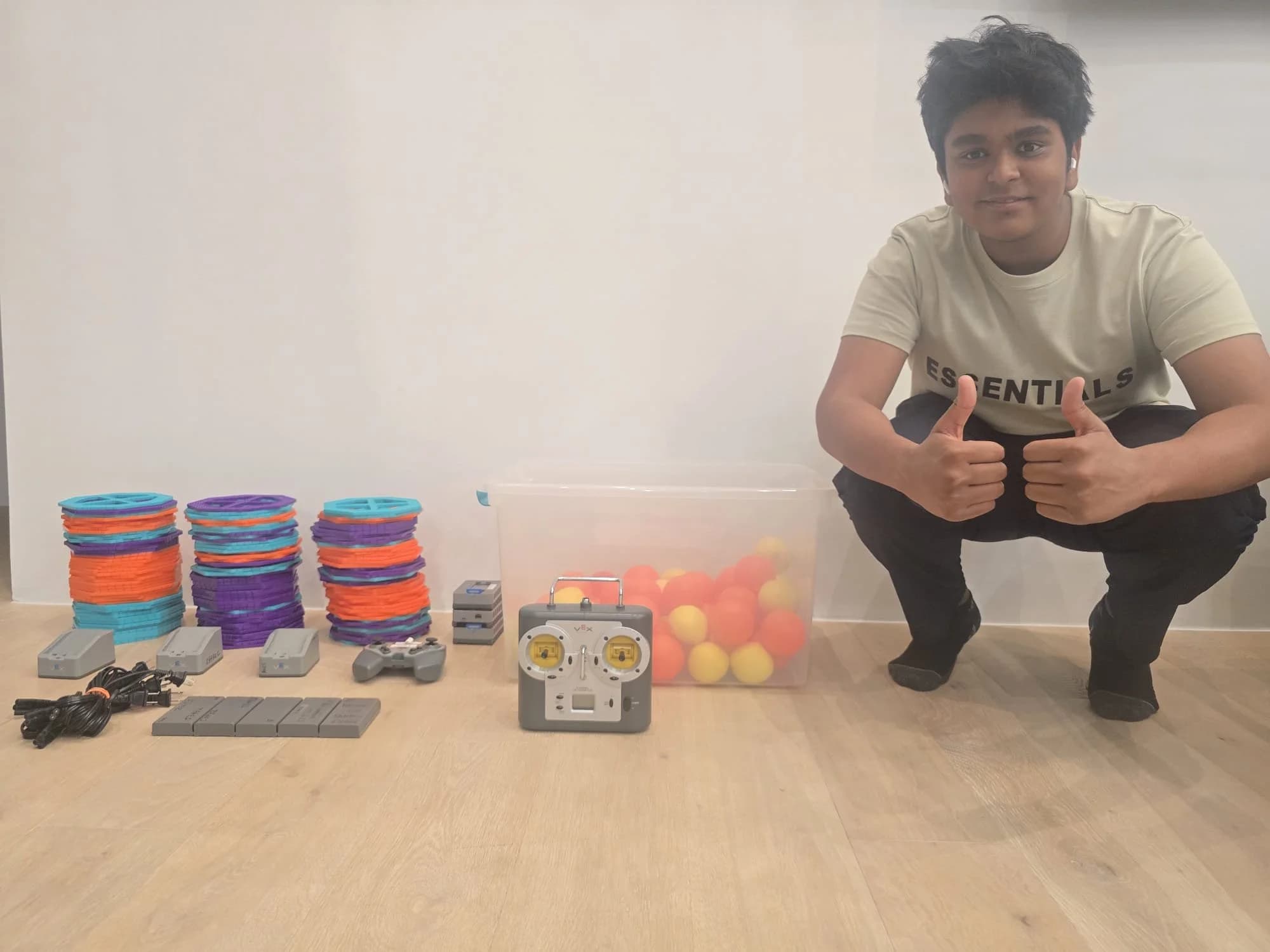 A volunteer giving a thumbs up next to donated VEX wheels, motors, a controller and a bin of game balls